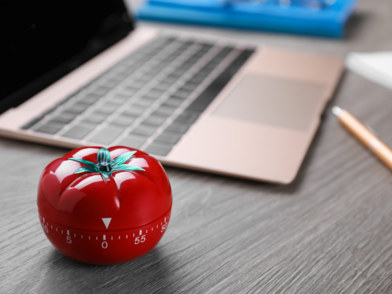 Photo of a pomodoro timer with a blurred image of a laptop and pen on a desk in the background