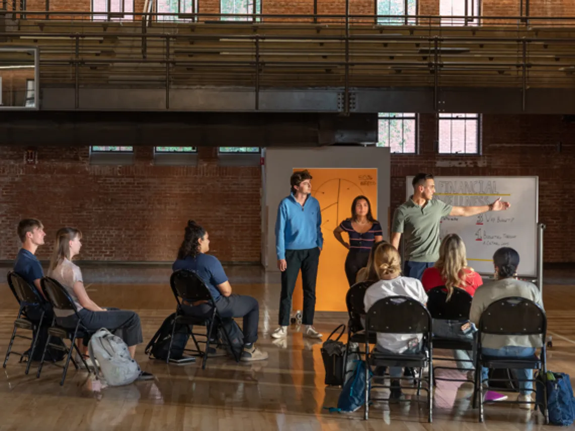 Group of students attending a group meeting on the Bear Down Gym floor.  Peer educator leads discussion in front of a rolling white board.