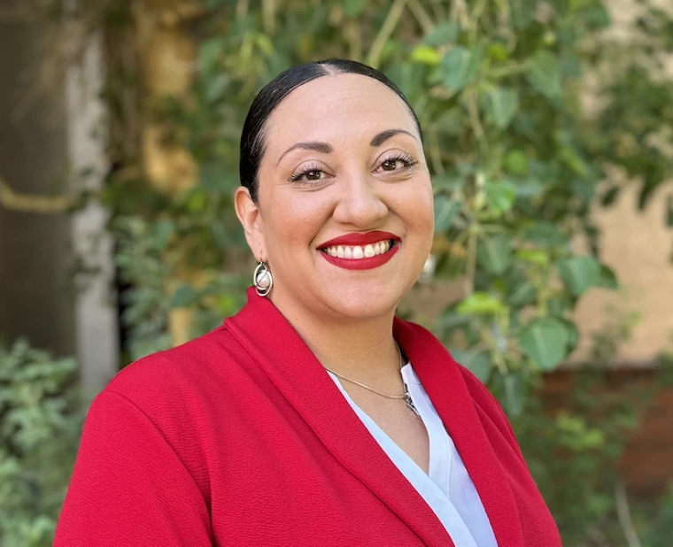 Michelle McKelvey in a red blazer in front of foliage. 