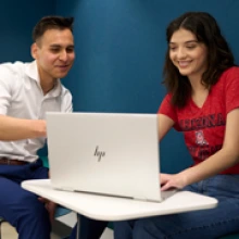 Two students sitting in front of a desk and talking.